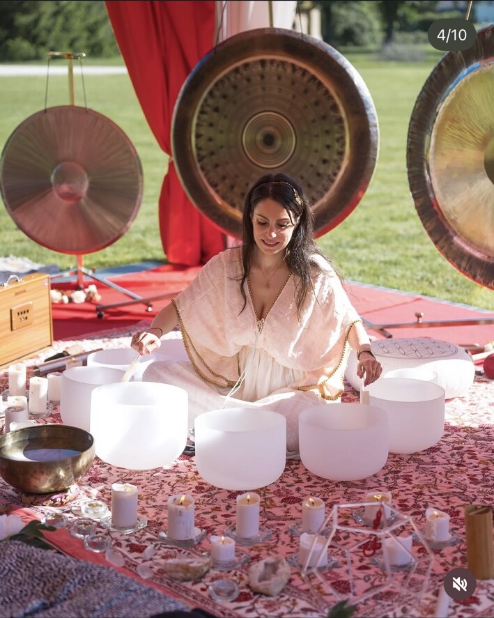 Mélanie Zadeh jouant des bols de cristal devant de grands gongs lors d’un bain sonore en plein air