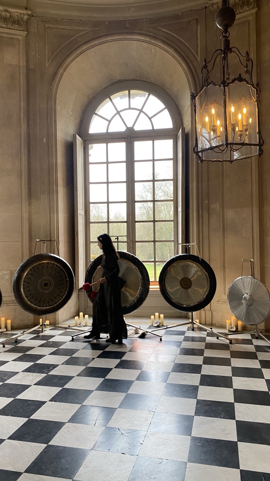 Mélanie Zadeh jouant devant une installation de gongs lors d’un événement dans un château